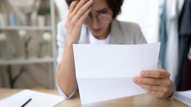 A woman holds a paper letter and looks sad and concerned at it